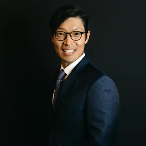 Dr. Eddie Lee in a navy suit and glasses, smiling.